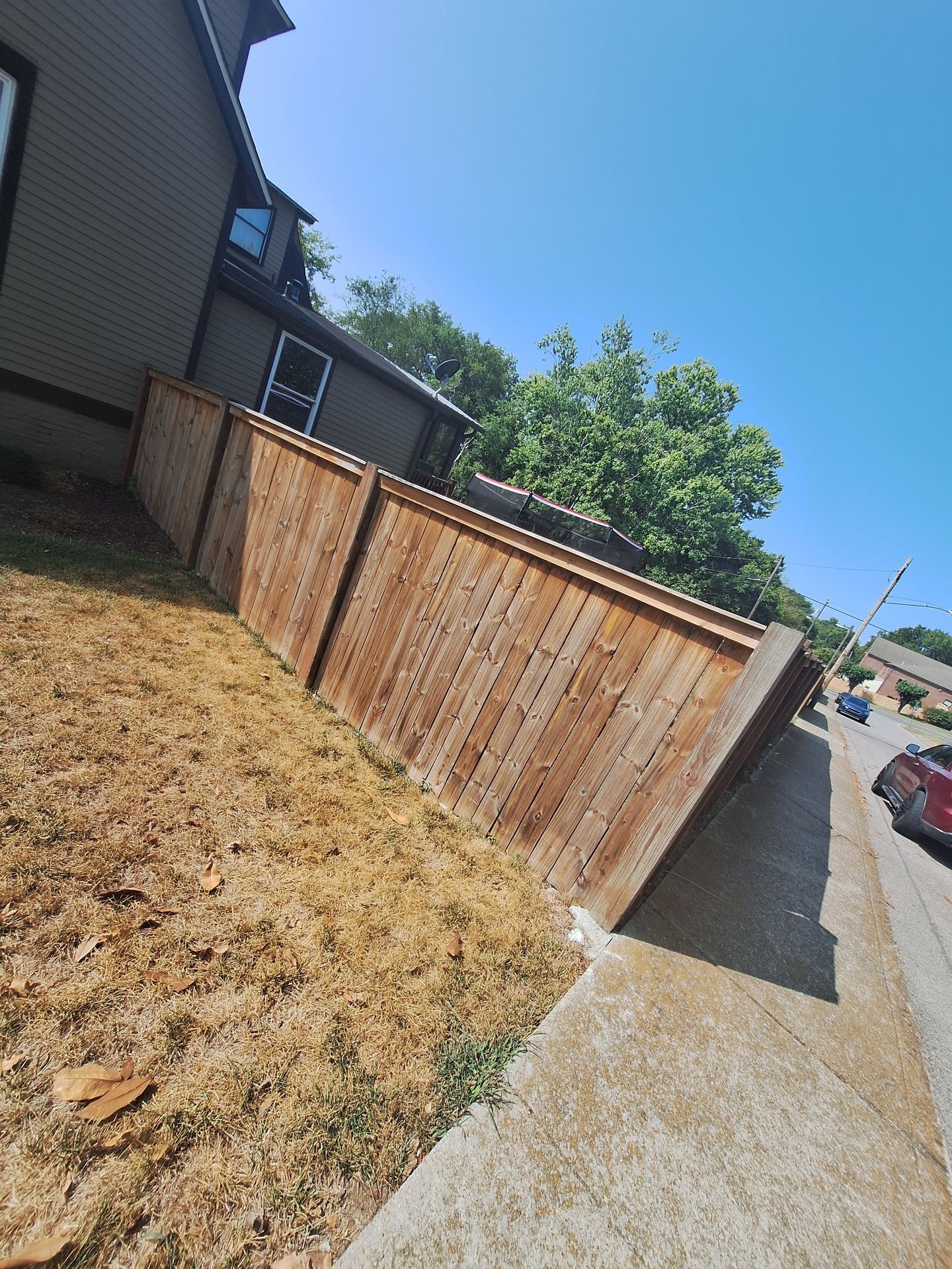 Wooden fence surrounding a house next to a dry lawn, under a clear blue sky.