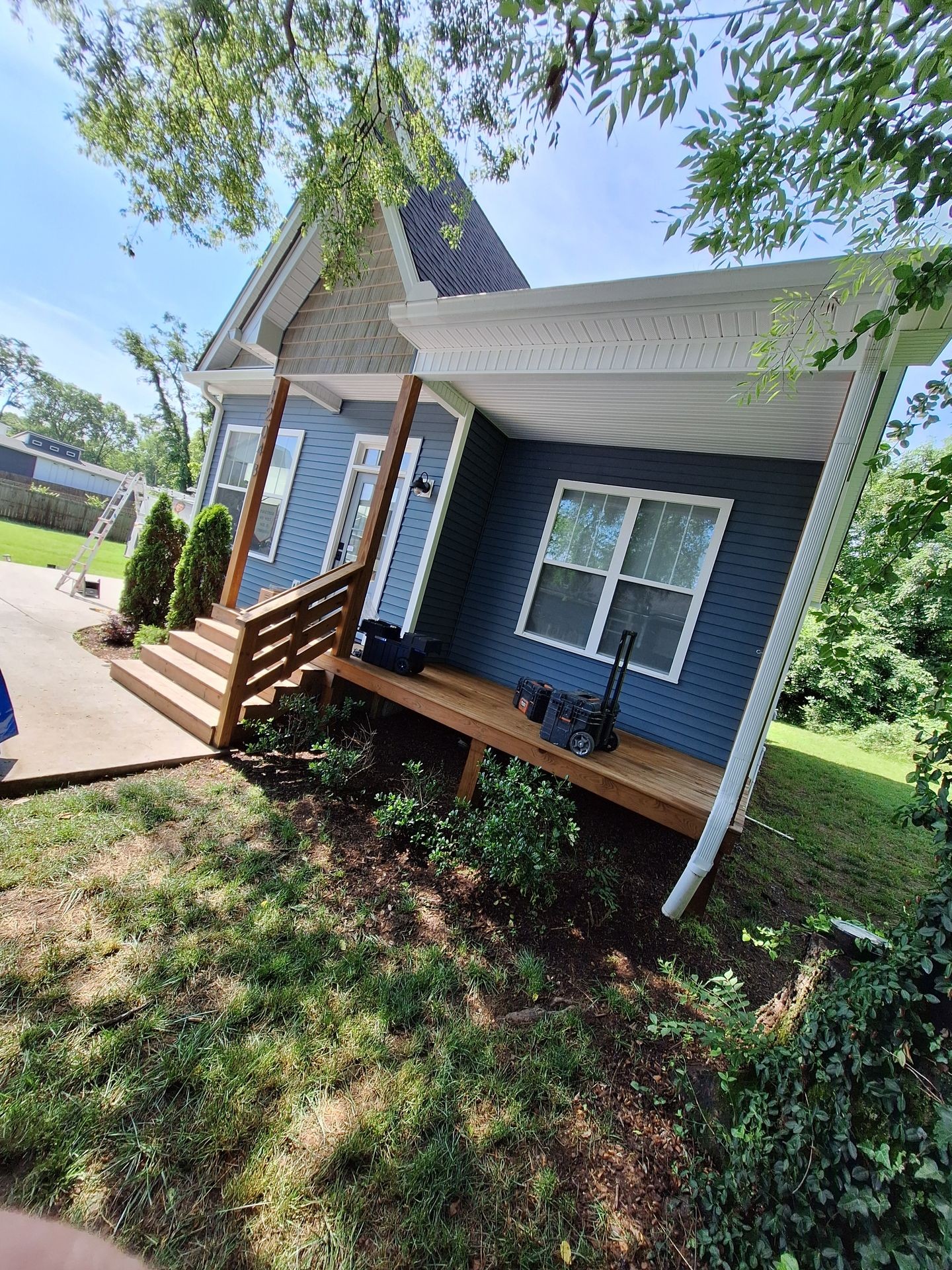 Blue house with a wooden porch, surrounded by greenery and a clear sky.