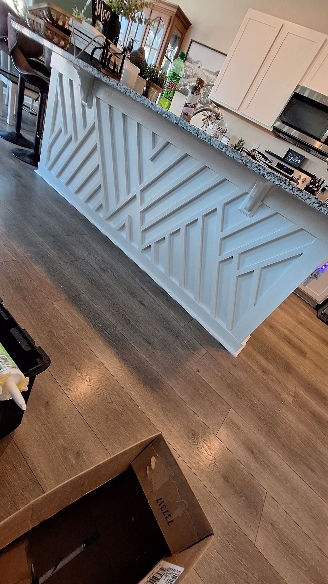 Modern kitchen island featuring a geometric patterned front panel and a granite countertop with various items on top.